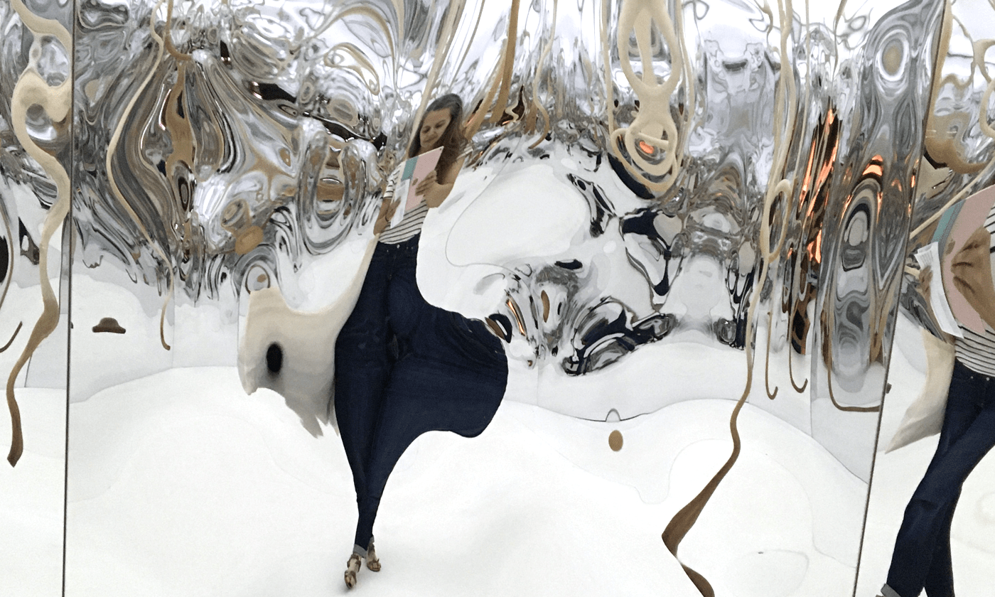 Woman reading inside a mirrored art installation with distorted reflections, evoking surprise and unexpected perspectives in the creative process